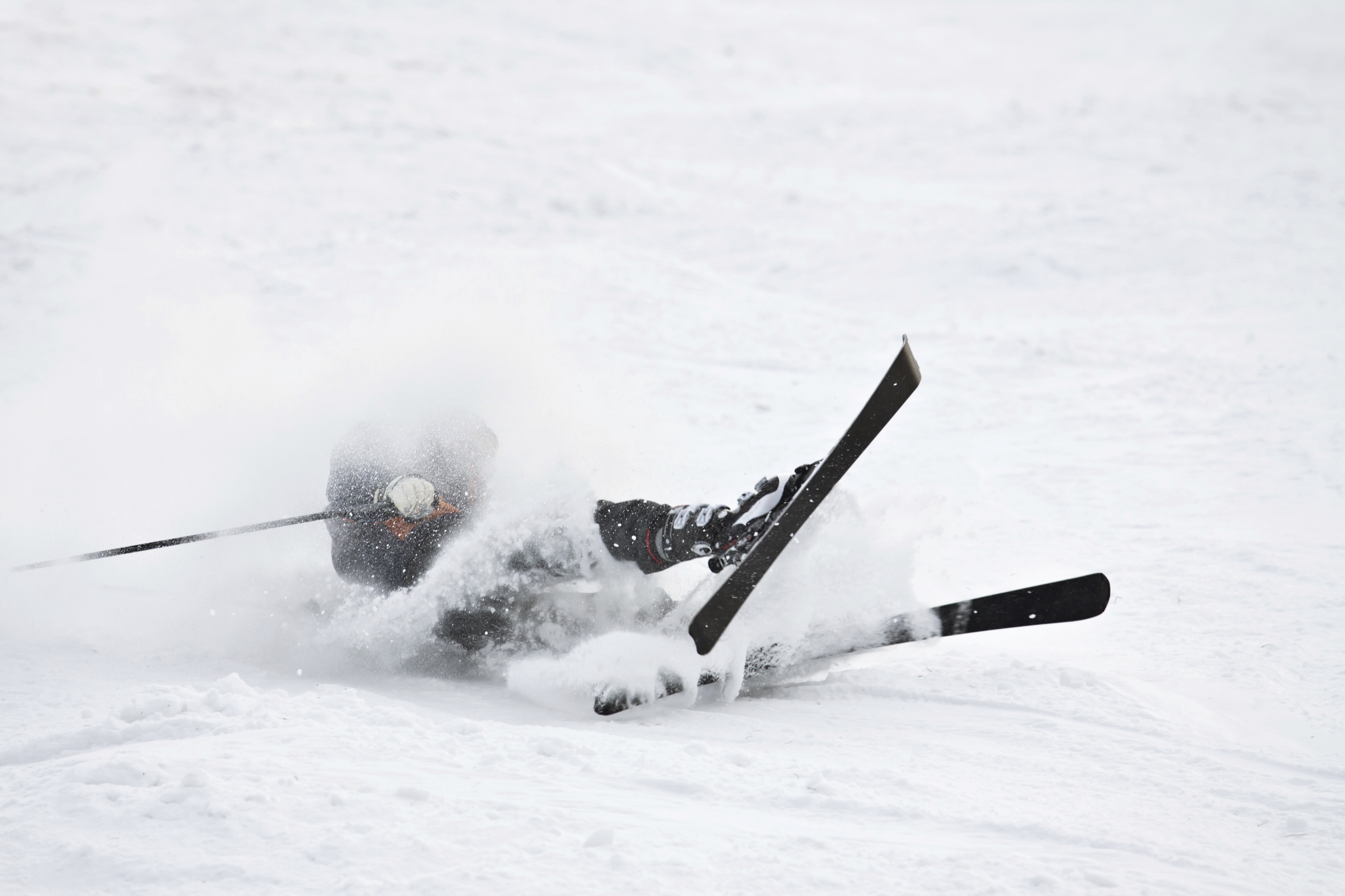 Ein Skifahrer stürzt auf einer Piste und ist umgeben von aufgewirbeltem Schnee.