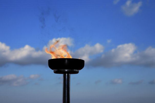 Die Olympische Fackel vor blauem Himmel mit einzelnen Wolken.