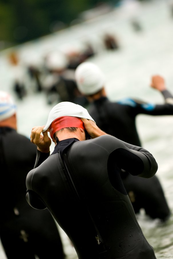 Schwimmstart bei einem Triathlon. Ein Schwimmer zieht sich gerade eine Badekappe über.