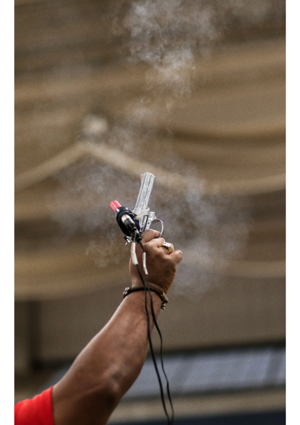 Eine Starterpistole, die den Start eines Wettkampfes anzeigt, wird in die Luft gehalten und gerade betätigt. Um die Pistole ist noch Rauch zu sehen. 