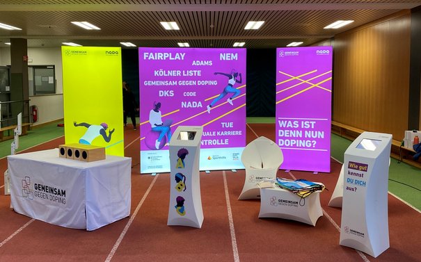 Ein Infostand von 'GEMEINSAM GEGEN DOPING' in einer Sporthalle.